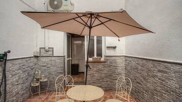 Un pequeño espacio al aire libre con mesa, sillas, una sombrilla y un equipo de aire acondicionado instalado en la pared.