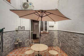 A small outdoor seating area with a table and chairs, an umbrella, and a wall-mounted air conditioning unit.