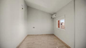 A room with a sloped ceiling, a window with a view of a building, and a light fixture on the wall.
