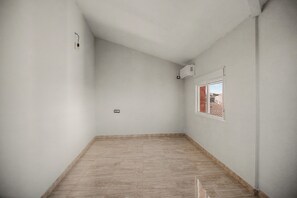 Une pièce avec un plafond en pente, une fenêtre donnant sur un immeuble et un luminaire fixé au mur.