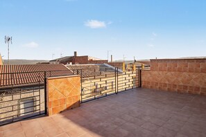 Una terraza en la azotea con suelo de baldosas, una reja metálica y vistas de los edificios circundantes.