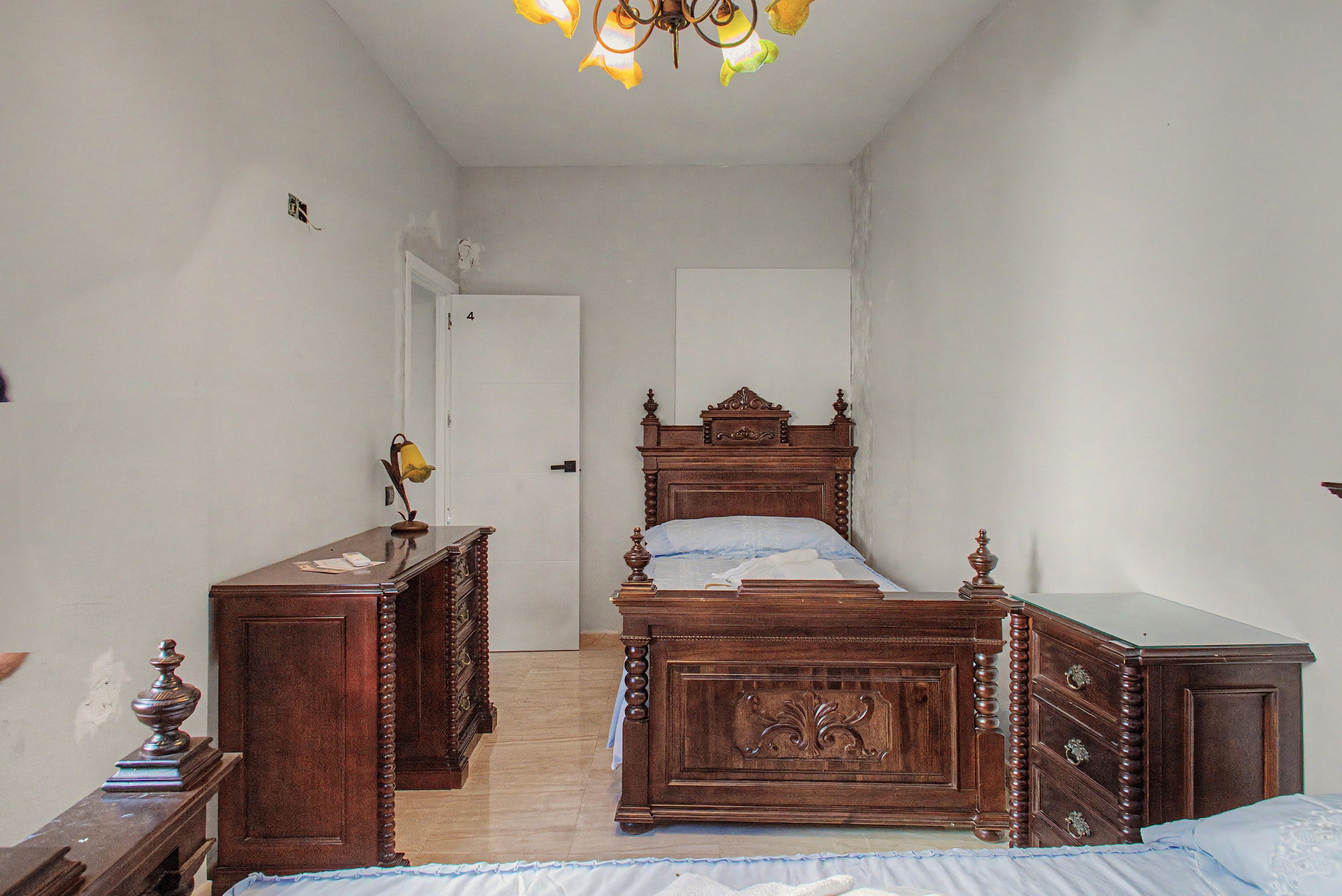 Une chambre à coucher avec un lit en bois, une commode, une table de chevet et une porte.