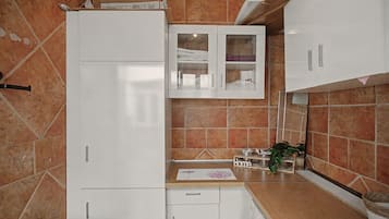 Cocina compacta con armarios blancos, horno integrado y una pequeña encimera con una planta.
