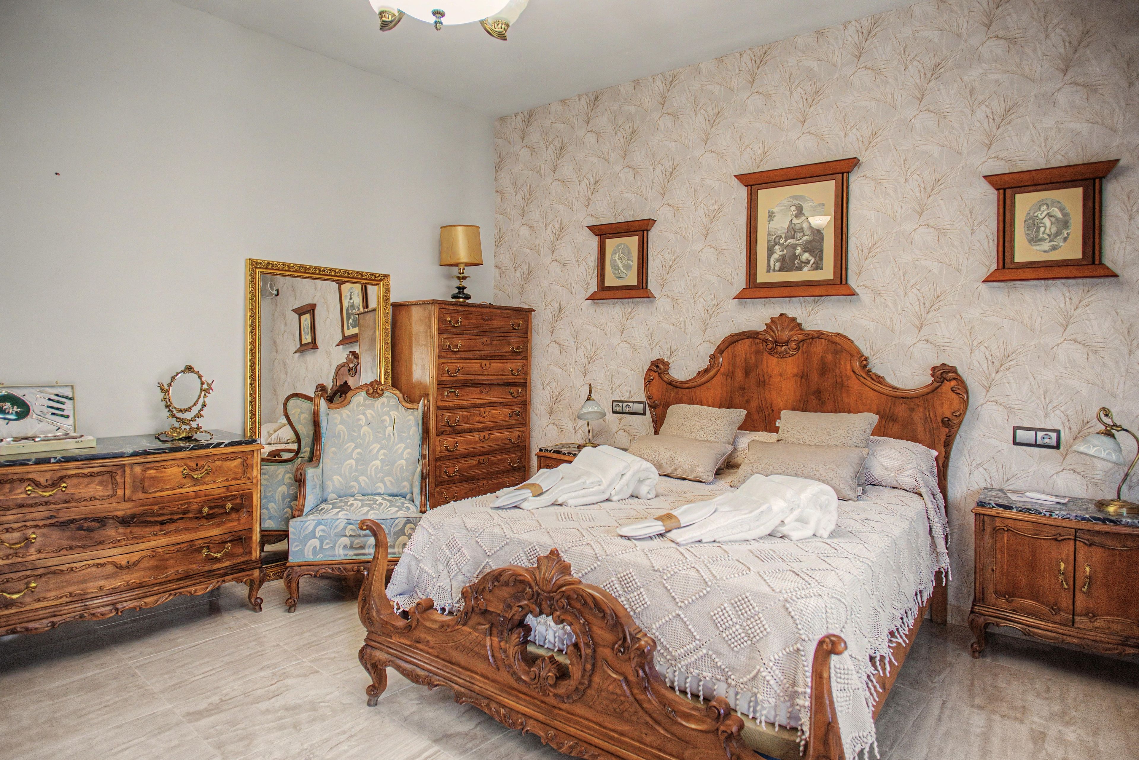 Un dormitorio clásico con una cama grande, un aparador, una silla y un espejo.