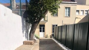 Un patio empedrado con un árbol, un edificio con una puerta y una valla.