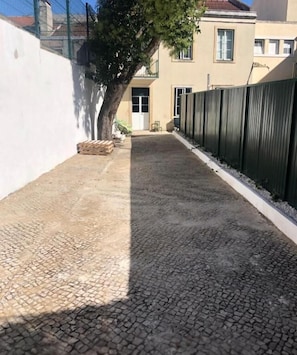 Un patio empedrado con un árbol, un edificio con una puerta y una valla.