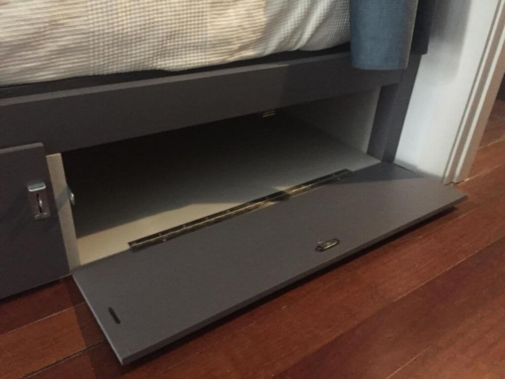 Un lit avec une tête de lit grise et un tiroir coulissant situé en dessous.