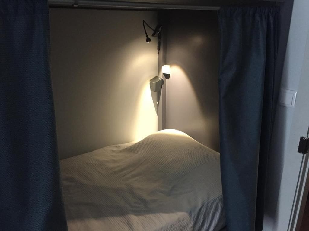 Ein Bett mit Kopfteil, einer Wandleuchte und Vorhängen.
