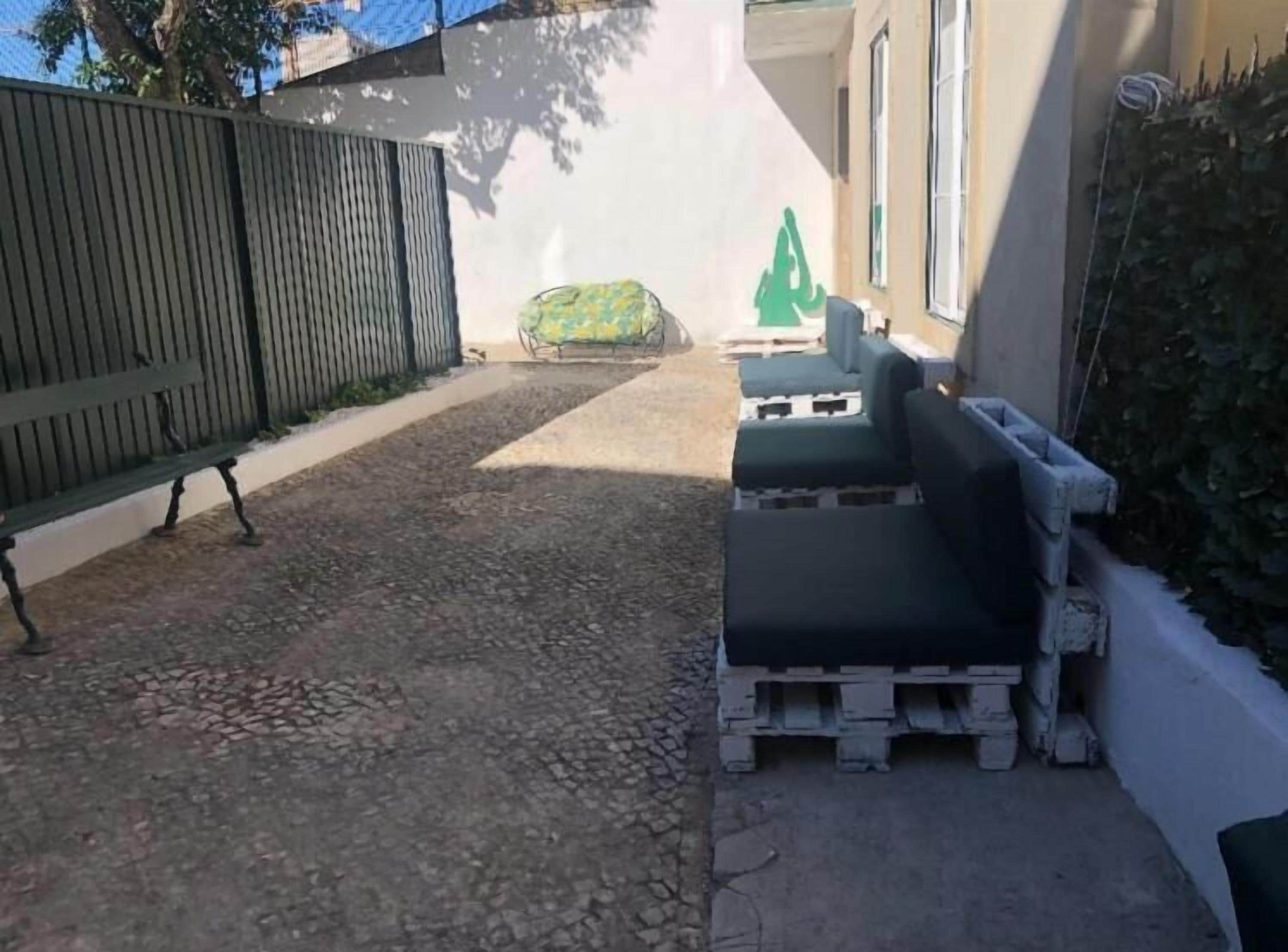 Un espace extérieur aménagé avec un revêtement, comprenant un banc et des sièges, une clôture et un bâtiment doté de fenêtres.