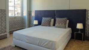 Un dormitorio con una cama grande, dos lámparas de noche, azulejos con diseño en la pared y un ventanal.