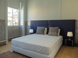 Un dormitorio con una cama grande, dos lámparas de noche, azulejos con diseño en la pared y un ventanal.