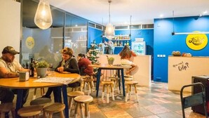 Un interior de restaurante con mesas, sillas, lámparas colgantes, una barra y una pared con un logotipo.