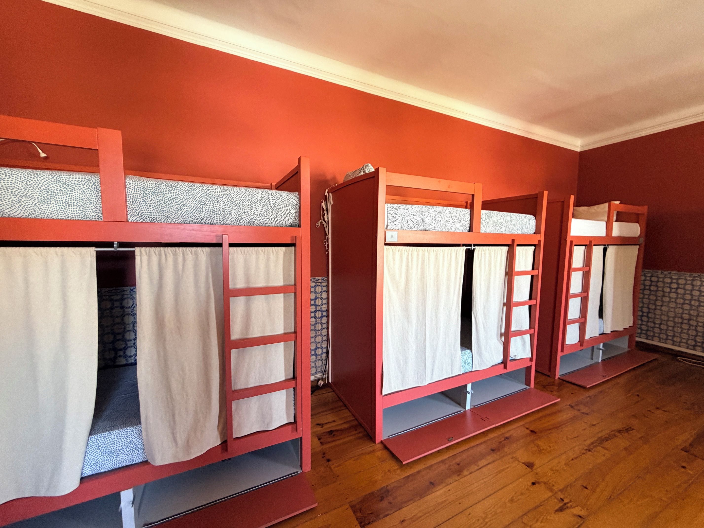Bunk beds with curtains and ladders, wooden flooring, and a red wall.