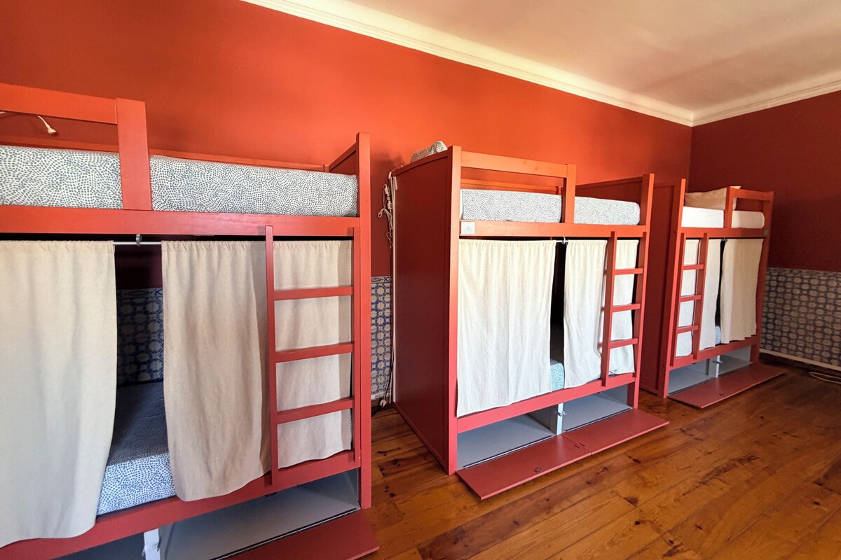 Camas literas con cortinas y escaleras, suelo de madera y una pared roja.