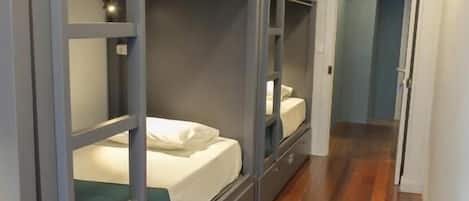 A corridor with bunk beds, wooden flooring, and a light fixture.