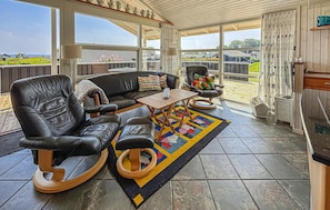 A sunroom with a black leather sofa, a wooden coffee table, and a view of the outdoors. - Stunning home in Sjølund with sauna (Sjølund)