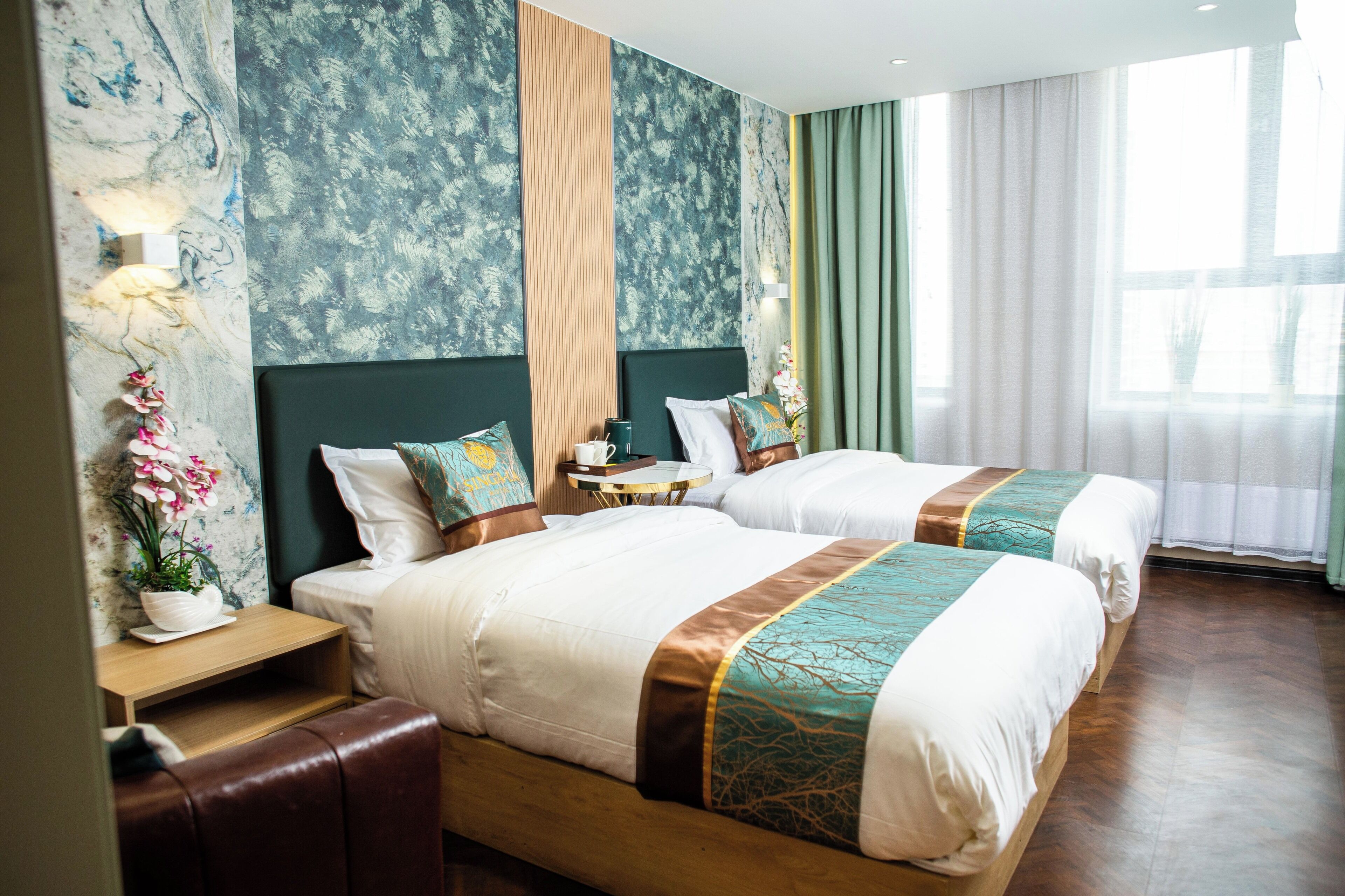 Habitación de hotel con dos camas, una mesita de noche, una lámpara y un ventanal con cortinas.