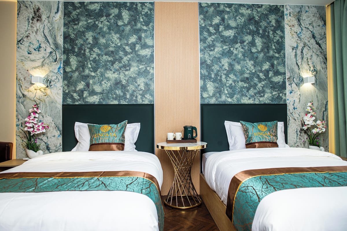 Habitación de hotel con dos camas, una mesa central y elementos decorativos como flores y cuadros.