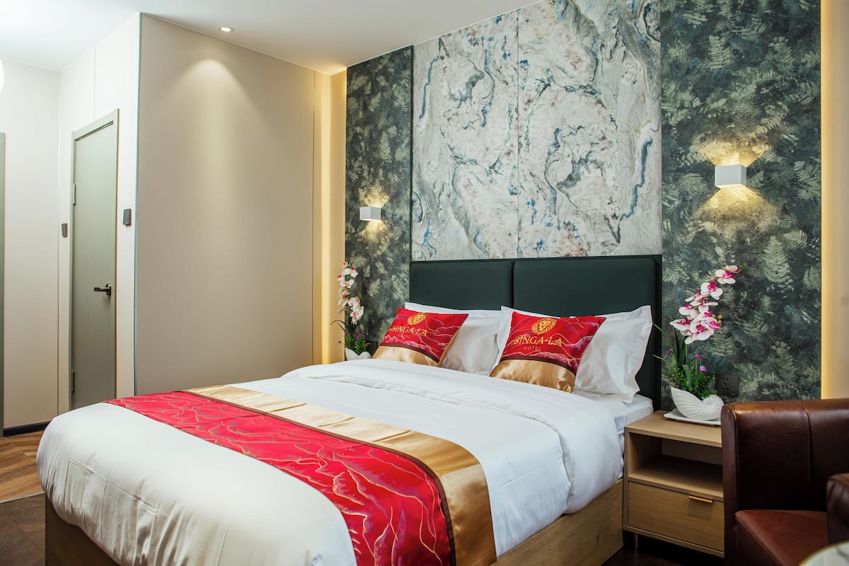 Una habitación de hotel con una cama, mesitas de noche, una silla y una pared de mármol.