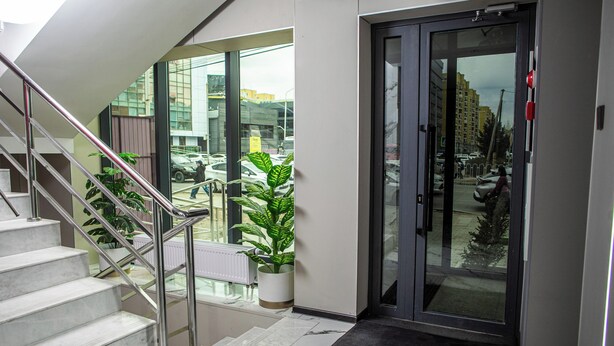 Een moderne hotelentree met een glazen deur, een trap met metalen leuningen en plantenpotten.