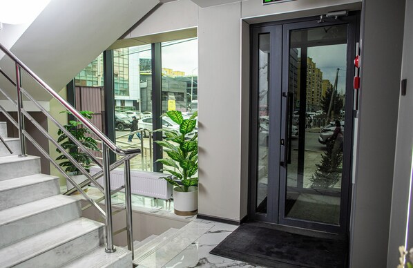 Una entrada de hotel moderna con puerta de cristal, escalera y plantas en macetas.