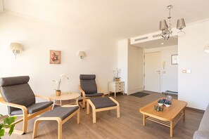 Una sala de estar moderna con un sofá, dos sillones, una mesa de centro y una mesita de noche con una lámpara y una planta.