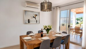 Un comedor con una mesa de madera dispuesta para seis personas, un cuadro en la pared y vistas a través de la puerta de vidrio.