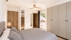 Un dormitorio con cama, ventilador de techo, armario y puerta corrediza de vidrio que da a un espacio exterior.