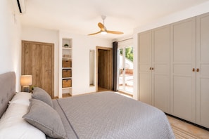 Ein Schlafzimmer mit Bett, Deckenventilator, Kleiderschrank und einer Glastür, die zu einem Außenbereich führt.