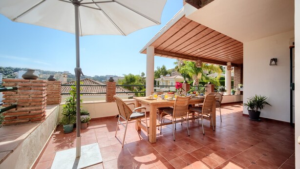 Un patio con una mesa y sillas, una planta en maceta y vistas de la ciudad.