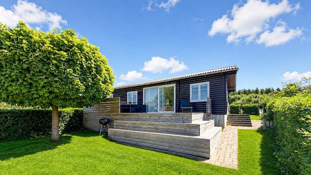 Ein modernes Blockhaus mit Terrasse, Grill und gepflegtem Rasen.