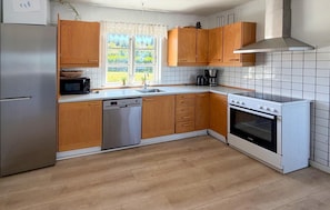 A kitchen with wooden cabinets, a dishwasher, a stove, and a window with a view of greenery. - 3 bedroom amazing home in Nordborg (Nordborg)