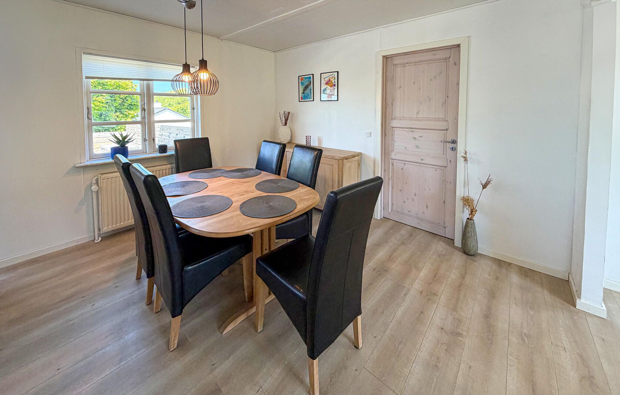 Uma área de refeições com uma mesa redonda de madeira, cadeiras pretas e um lustre.