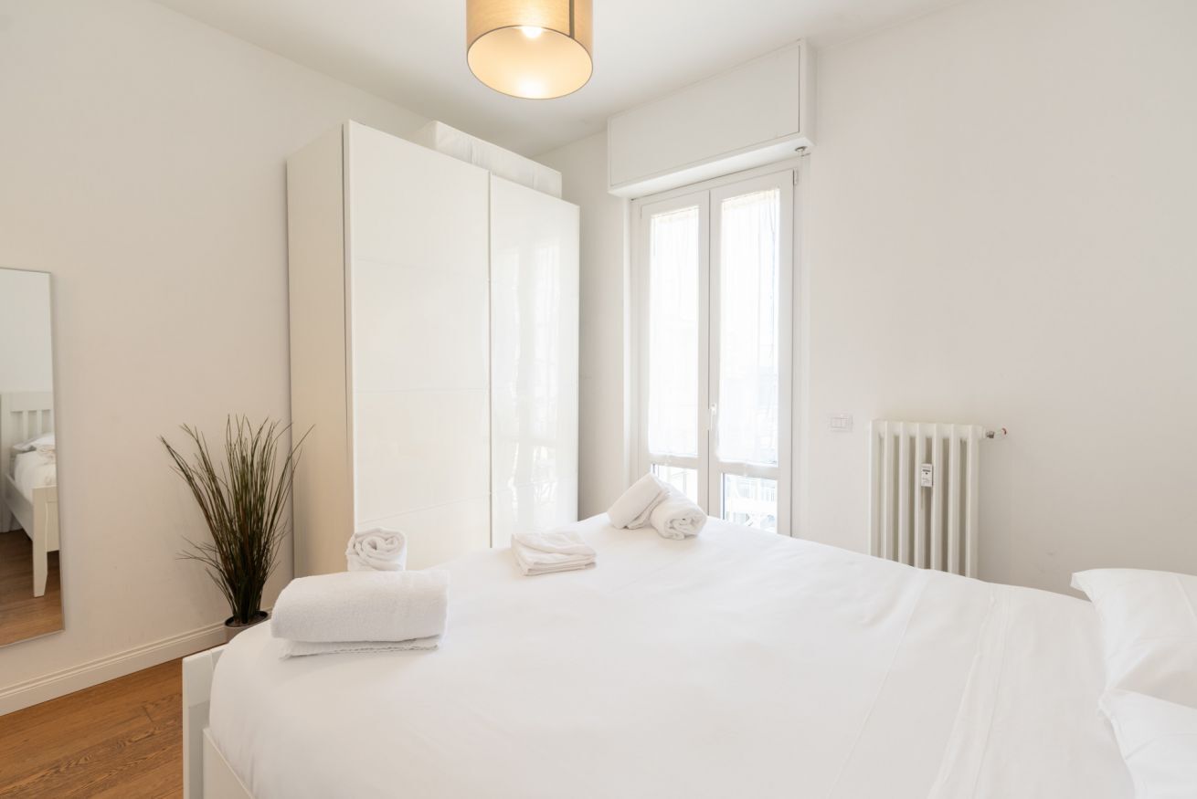 A bedroom with a large bed, a radiator, a window, and a mirror.
