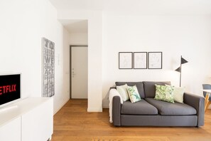 Ein modernes Wohnzimmer mit grauem Sofa, einem Flachbildfernseher und gerahmten Kunstwerken an der Wand.