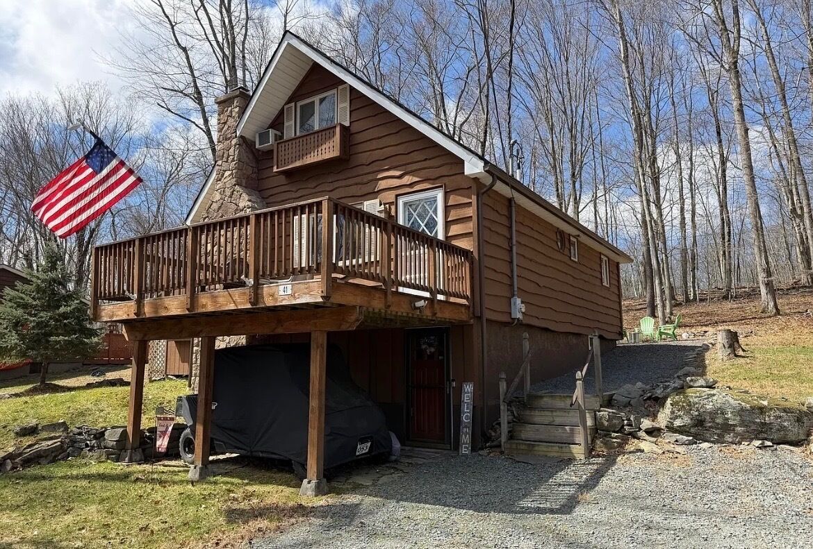 Een chalet van twee verdiepingen met een balkon, een garage en een welkomstbord.