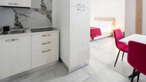Une cuisine moderne avec un dosseret en marbre, un coin repas avec des chaises rouges et une chambre à coucher avec un lit et une table de chevet.
