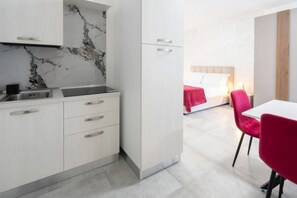 Una cucina moderna con zoccolo in marmo, un'area pranzo con sedie rosse e una camera da letto con un letto e un comodino.