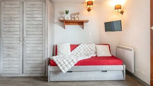 Una camera da letto con un letto, un armadio, una mensola con oggetti decorativi, una TV a parete e una lampada a parete.