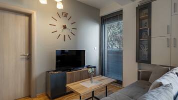 Een moderne woonkamer met een flatscreen televisie, een houten salontafel, een bank, een inbouw boekenkast en een wandklok.