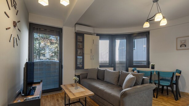 Een moderne woonkamer met een bank, salontafel, televisie en een eethoek met stoelen.