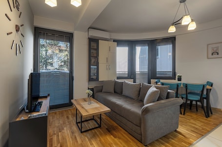 A modern living room with a sofa, a coffee table, a TV, and a dining area with chairs.. La Vita Apartment 1 by Sienna