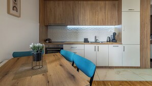 Een moderne keuken met houten kastjes, een witte koelkast en een eettafel met blauwe stoelen.