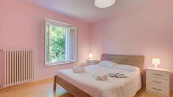 Un dormitorio con cama de madera, dos mesitas de noche con lámparas, una ventana y un radiador.