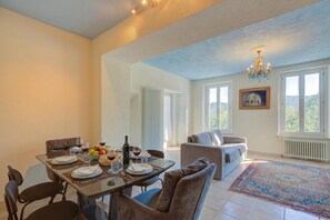 A dining area with a table set for four, a sofa, a chandelier, and a view of the outdoors. - Villa Lake View With BBQ (Lugano)