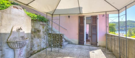 Un espacio al aire libre cubierto con suelo de piedra, un jarro decorativo, una reja de metal y una pared rosa con una puerta.