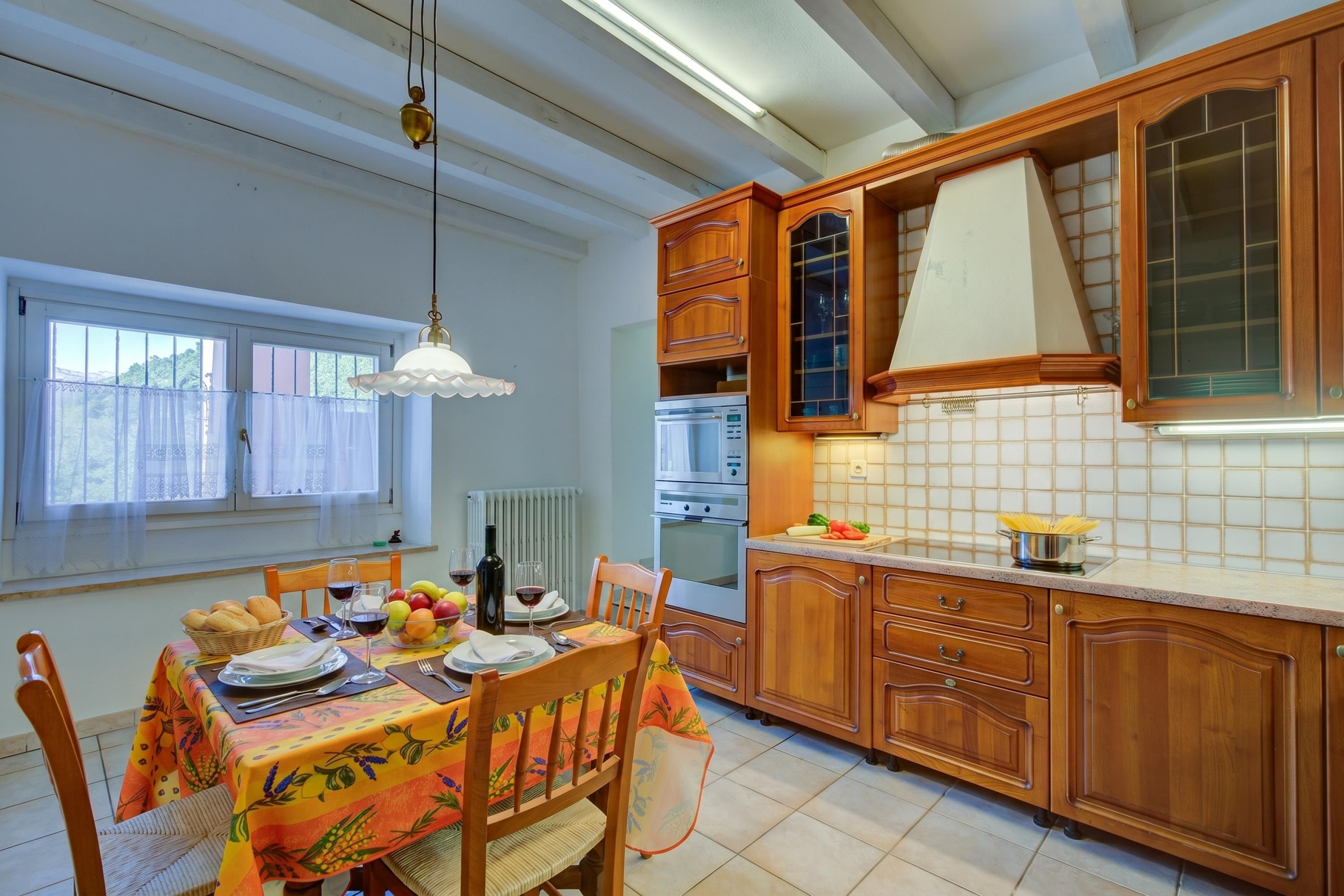 A kitchen with wooden cabinets, a dining table set with plates, glasses, and a bottle.