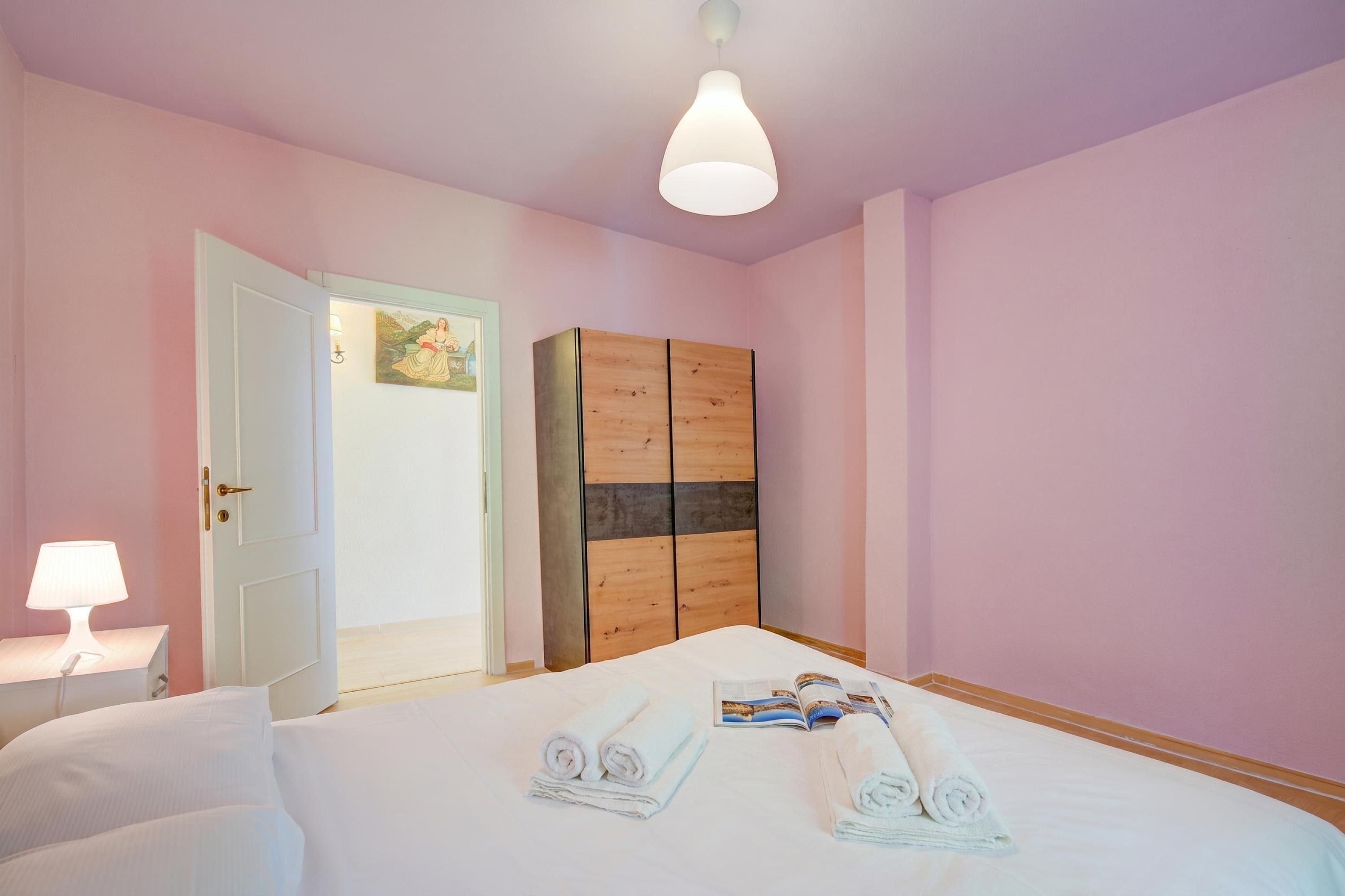 Une chambre à coucher avec un lit, une table de chevet avec une lampe, une armoire en bois et une porte donnant sur une autre pièce.