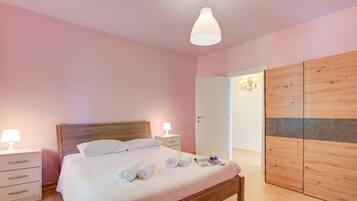 Una camera da letto con un letto in legno, comodini con lampade, un armadio in legno e una porta che conduce a un'altra stanza.