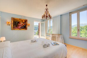 Un dormitorio con cama, un candelabro, un cuadro y vistas por la ventana.